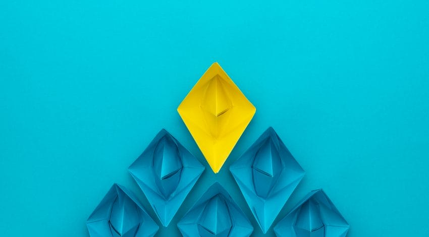 A yellow paper boat leading blue paper boats